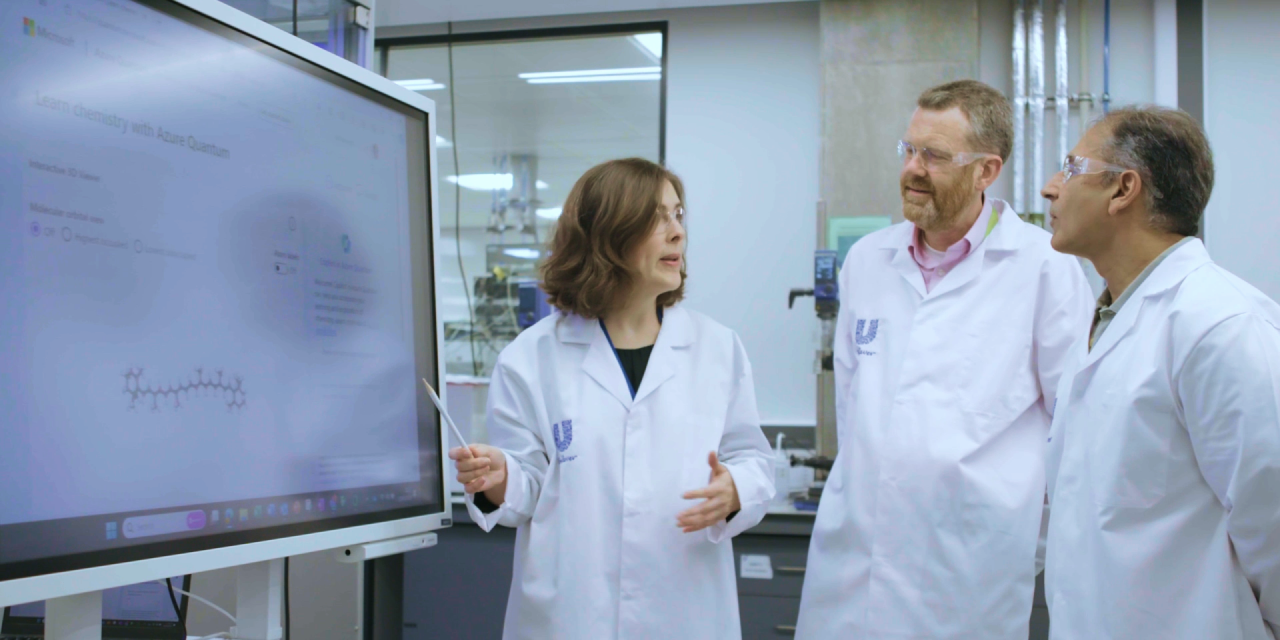 One woman and two men in while lab coats looking at a computer screen featuring Microsoft Azure Quantum Elements.