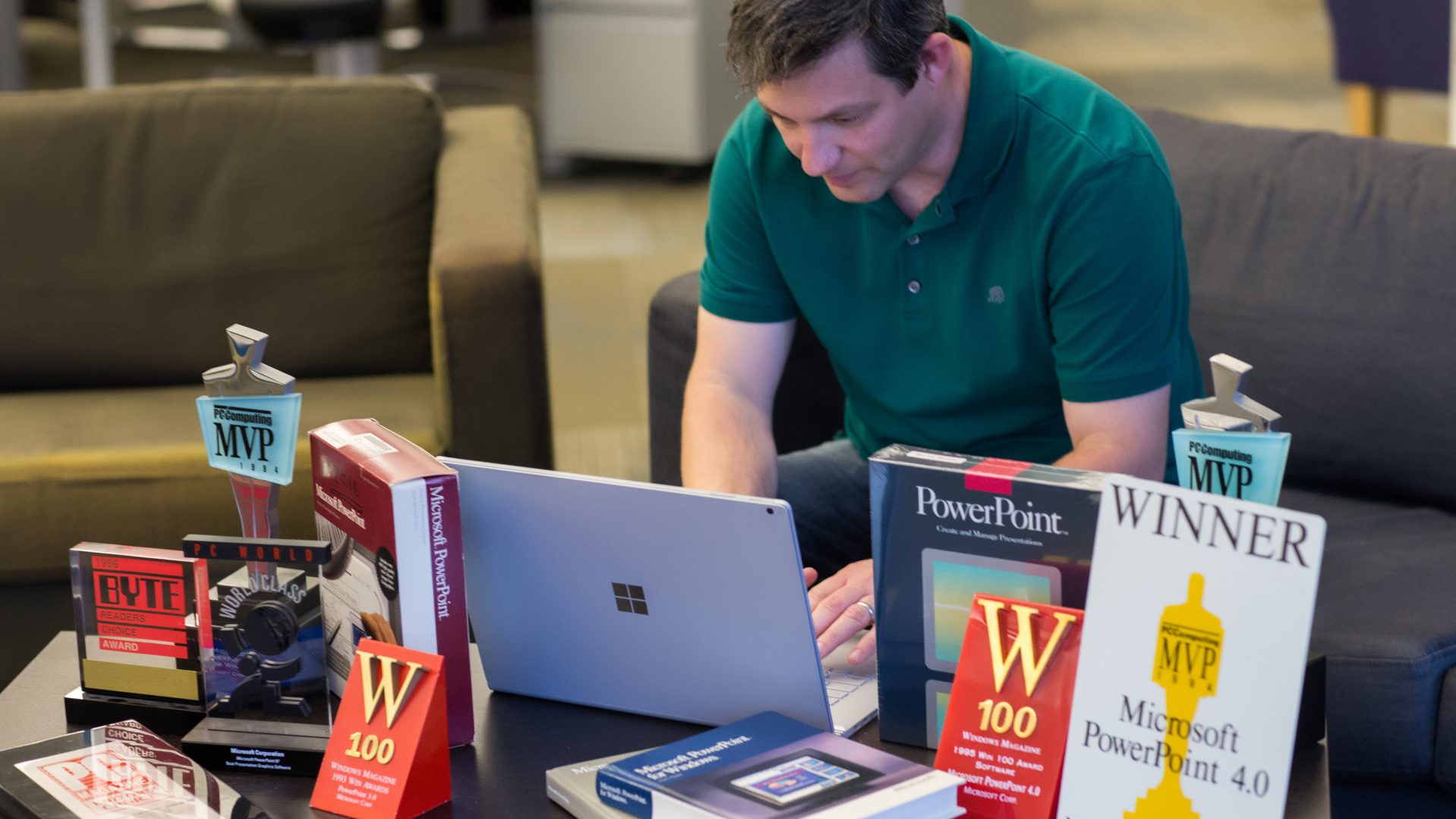 Shawn Villaron using a laptop and surrounded by PowerPoint awards.