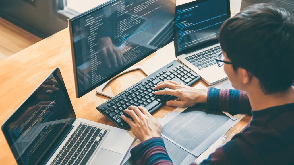 Person using a desktop computer and two laptops.